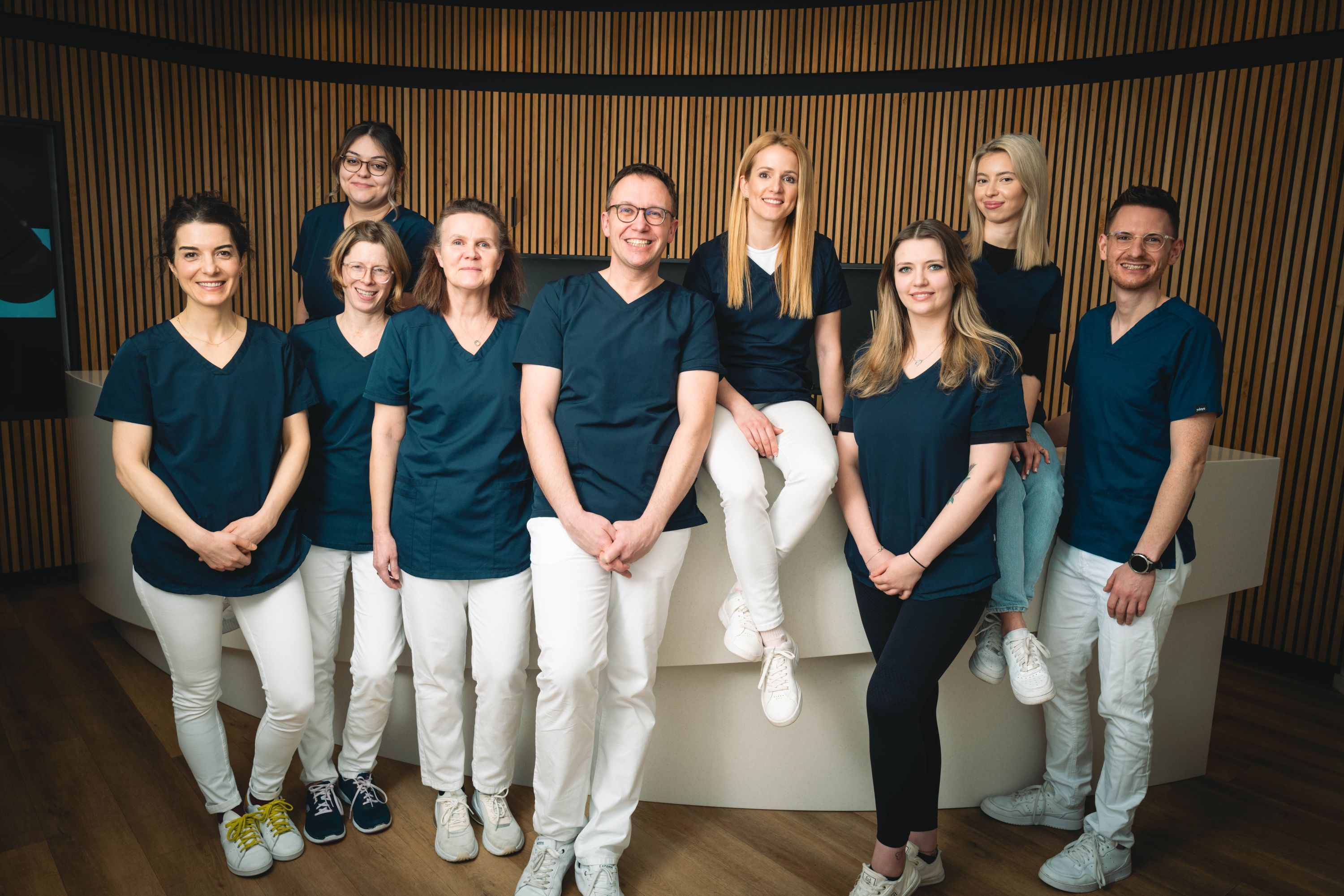 Gruppenfoto der 9 Mitarbeiterinnen und Mitarbeiter in dunkelblaugrauen Shirts und weißen Hosen